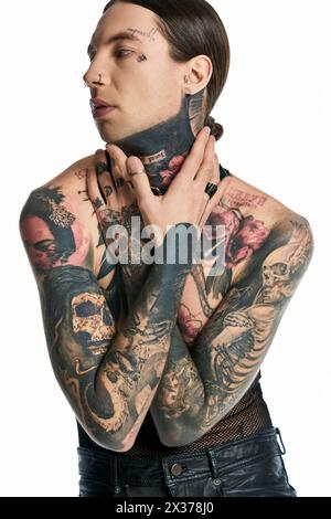 Un jeune homme avec des tatouages complexes ornant sa poitrine et son cou pose élégamment dans un studio sur un fond gris. Banque D'Images