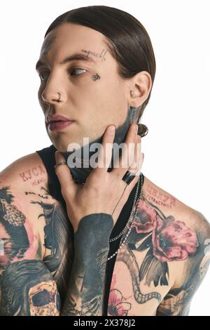 Un jeune homme élégant avec une variété de tatouages couvrant son corps et son cou, posant dans un studio sur un fond gris. Banque D'Images