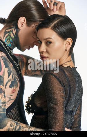 Un jeune homme et une femme élégants avec des tatouages de bras complexes posant dans un studio sur un fond gris. Banque D'Images