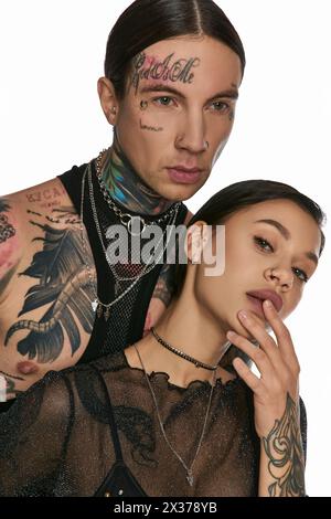 Un jeune homme et une jeune femme avec des tatouages complexes sur leurs visages posent dans un studio sur un fond gris. Banque D'Images