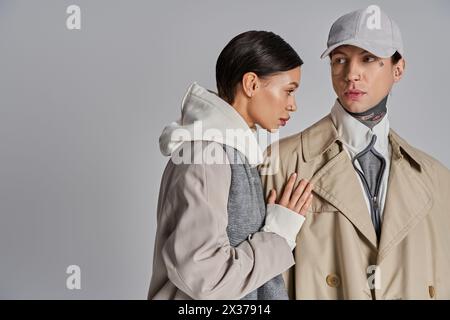 Un jeune homme et une jeune femme portant des trench-coat se tiennent côte à côte dans un studio sur un fond gris. Banque D'Images