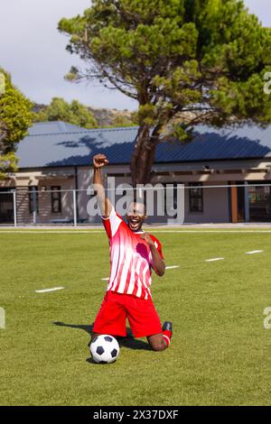 Jeune athlète masculin afro-américain en rouge et blanc célébrant sur le terrain de football, espace copie Banque D'Images