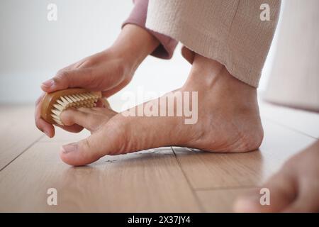 À l'aide d'une brosse, la personne brosse doucement son pied sur le plancher de bois franc Banque D'Images