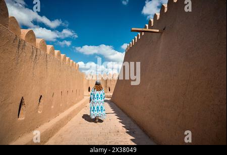 Jeune femme en robe ethnique avec ornement bleu marchant au mur de la ville dans Itchan Kala ancienne ville de Khiva en Ouzbékistan. Banque D'Images