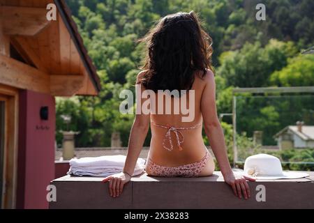 vue arrière d'une jeune femme assise sur un rebord regardant les montagnes avec une serviette et un chapeau. Banque D'Images