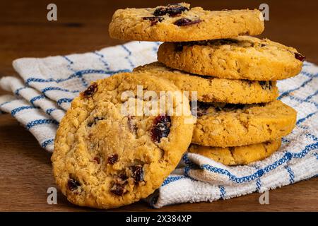 Pile de flocons d'avoine faits maison et biscuits aux canneberges sur un torchon blanc sur une table en bois. Banque D'Images