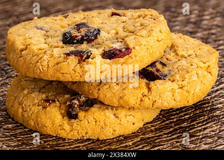 Pile extrême gros plan de flocons d'avoine circulaires croustillants et biscuits aux canneberges sur un tapis de table foncé. Banque D'Images