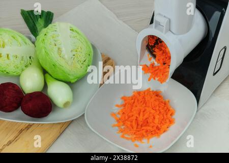 Carotte, betteraves, oignon et chou dans un coupe-légumes sur la table de la cuisine. La carotte hachée tombe dans un bol. Cuisine maison. Ligne de santé. Banque D'Images