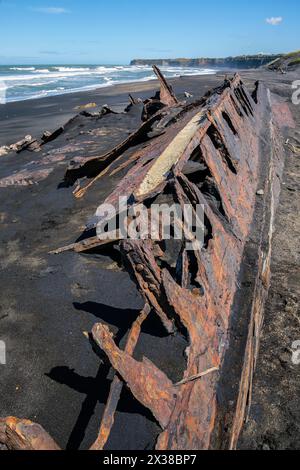 La coque rouillée d'un bateau à moitié enterré dans le sable noir de Patea Beach, Taranaki, Île du Nord, Nouvelle-Zélande Banque D'Images