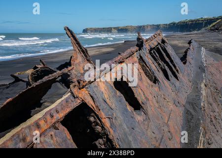 La coque rouillée d'un bateau à moitié enterré dans le sable noir de Patea Beach, Taranaki, Île du Nord, Nouvelle-Zélande Banque D'Images