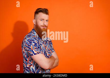 Photo de profil de côté de la chemise imprimée confiante Serious brutal Man Wear tenant les bras croisés isolé sur fond de couleur orange vif Banque D'Images