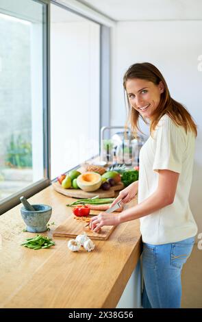 Portrait, maison et femme avec des légumes, coupe et sourire avec végétalien, repas sain et nutrition. Visage, végétarien et personne dans la cuisine, la nourriture et Banque D'Images