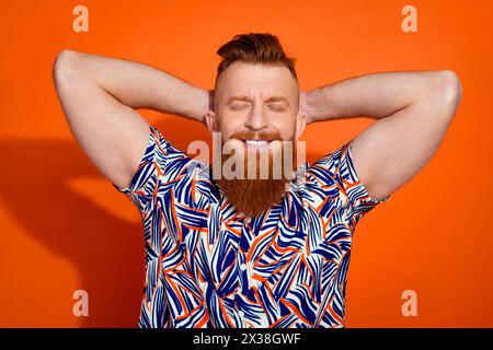 Photo de Good Mood Dreamy Guy Dressed Print Chemise bras derrière la tête les yeux fermés isolé fond de couleur orange Banque D'Images