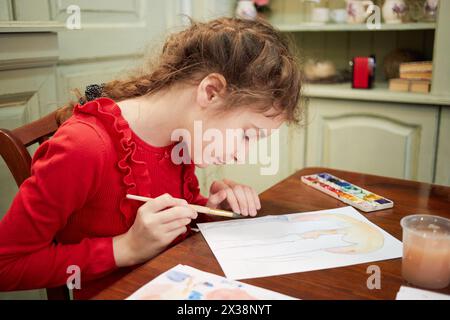 Fille dessine des aquarelles assis à table dans la chambre. Banque D'Images