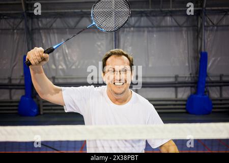 Homme souriant dans des lunettes avec raquette de badminton au terrain de sport. Banque D'Images