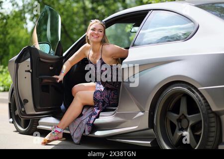 Fille heureuse avec de longs cheveux dans une robe d'été hors d'une voiture de sport Banque D'Images