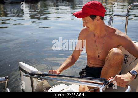 Homme dans le chapeau regarde l'eau sur yacht pendant la voile sur la rivière à la journée ensoleillée d'été Banque D'Images