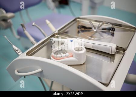 Modèle de mâchoire humaine avec dents, brosse à dents électrique et lunettes au cabinet de dentiste, dof peu profond. Banque D'Images