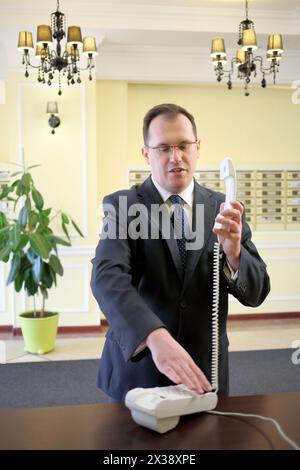 Homme dans un costume d'affaires tenant un téléphone et compose le numéro dans le couloir de l'immeuble de luxe Banque D'Images