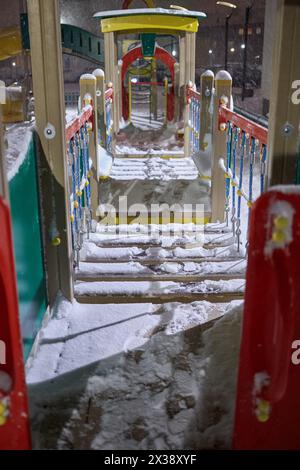 Construction en bois recouverte de neige sur le terrain de jeux dans la cour sous les chutes de neige du soir. Banque D'Images