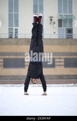 L'homme se tient sur les mains à l'envers à côté du bâtiment le jour d'hiver Banque D'Images