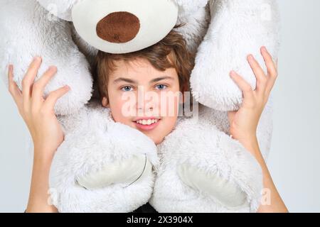 Garçon adolescent dans des poses grises avec un grand ours blanc jouet en studio Banque D'Images