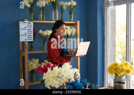 Portrait de femme d'affaires propriétaire de magasin floral debout tenant l'ordinateur portable à la main, regardant la caméra. Fleuriste féminine travaillant en utilisant l'ordinateur dans ses fleurs Banque D'Images