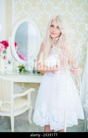 Jeune femme en robe blanche touche cintre blanc dans une pièce lumineuse confortable Banque D'Images