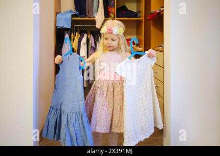 Petite blonde jolie fille dans la couronne choisit robe dans la garde-robe à la maison Banque D'Images