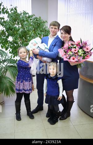 Jeune homme avec nouveau-né, femme avec des fleurs et deux filles à la maternité Banque D'Images