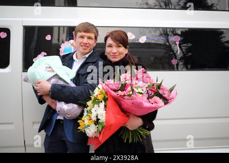 Homme avec nouveau-né, femme avec des fleurs se tiennent près de la limousine blanche festive en plein air Banque D'Images