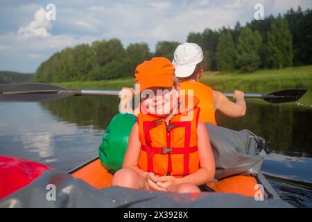 Heureux petit garçon et femme dans les gilets de sauvetage naviguent sur bateau gonflable sur la rivière à l'été, concentrez-vous sur l'enfant Banque D'Images