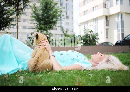 Blonde avec veau de lion se trouve sur l'herbe près du bâtiment le jour d'été Banque D'Images