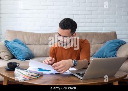 Jeune homme architecte indépendant ou designer d'intérieur travaillant seul à partir d'un petit bureau à domicile confortable. Homme indépendant éduqué et créatif utilisant ordinateur portable comp Banque D'Images