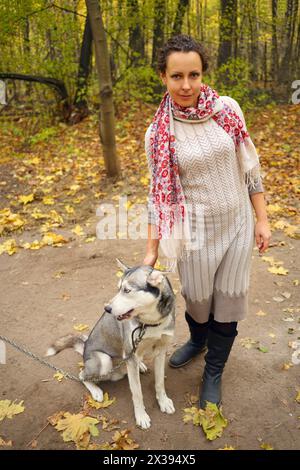 Jolie femme se tient près du chien Husky dans la forêt sèche d'automne, corps entier Banque D'Images