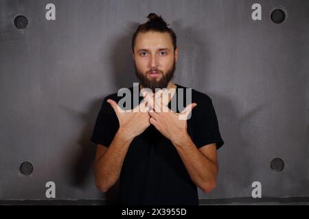 Bel homme à la mode avec la barbe pose dans le studio près du mur Banque D'Images