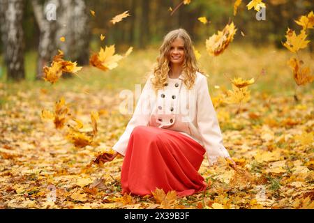 Belle jeune femme en jupe rouge jette des feuilles dans le parc d'automne jaune Banque D'Images