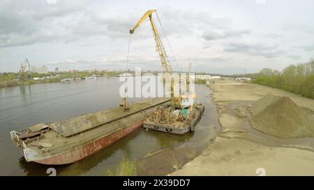 SAMARA - 10 MAI 2015 : grue et barge pour le sable sur la rive de la rivière Volga au printemps jour nuageux. Image vidéo de vue aérienne Banque D'Images