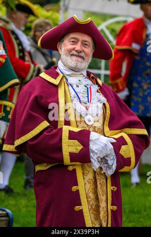 Town crier pose, debout regardant la caméra, donnant le sourire (livrée tressée colorée du crieur, médaille autour du cou) - Ilkley, West Yorkshire, Angleterre Royaume-Uni. Banque D'Images