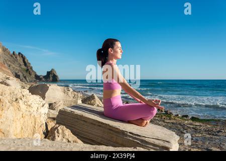femme sportive pratiquant le yoga et méditant sur les rochers au bord de la mer. Banque D'Images