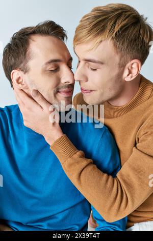 Deux hommes en tenue décontractée s'embrassant tendrement sur un fond gris. Banque D'Images