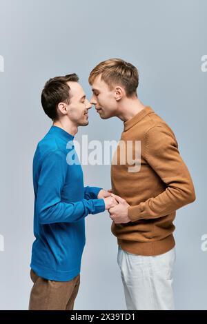 Deux jeunes hommes, un couple gay aimant, se tiennent ensemble dans une tenue décontractée sur un fond gris. Banque D'Images