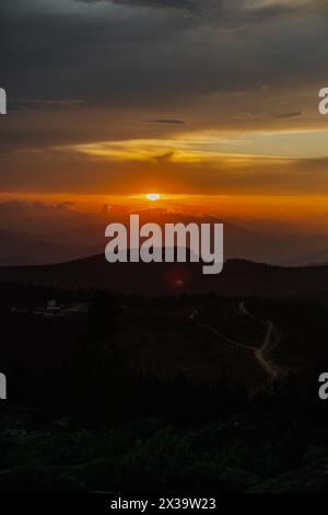 Le soleil plonge sous l'horizon, projetant une lueur chaude sur une chaîne de montagnes accidentée au loin. Banque D'Images