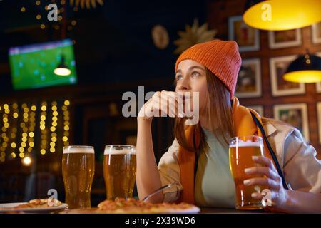 Mignonne femme fan de football regardant le match de télévision dans le bar des sports Banque D'Images