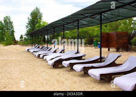 Zone de loisirs de plage sur la rive du lac. Des transats vides se tiennent sur le sable. La plage attend les touristes. Banque D'Images