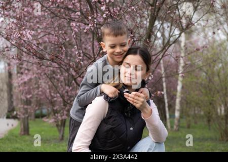 Fils donne à sa mère une petite fleur de cerisier en fleur au printemps Banque D'Images