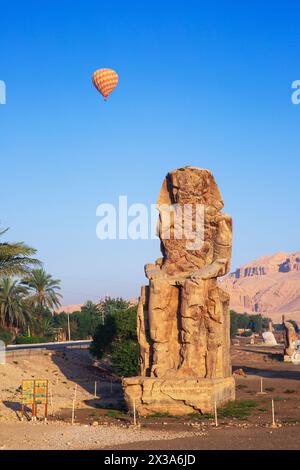 Une montgolfière colorée survolant les colosses de Memnon au lever du soleil sur la Cisjordanie de Louxor, en Égypte Banque D'Images