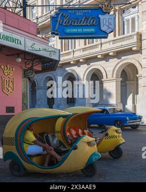 Deux taxis coco jaune vif stationnés à l’extérieur du Floridita Bar, l’un des repaires d’Ernest Hemmingway dans la vieille Havane, la Havane, Cuba. Banque D'Images
