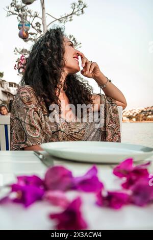 belle femme méditerranéenne aux cheveux bouclés sourit assis à une table de restaurant Banque D'Images