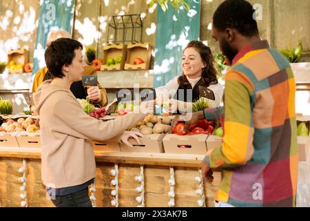 Commerçant amical souriant offrant au client de goûter des variétés de pommes fraîches de saison au marché alimentaire. Heureuse agricultrice vendant des fruits et légumes biologiques locaux. Banque D'Images